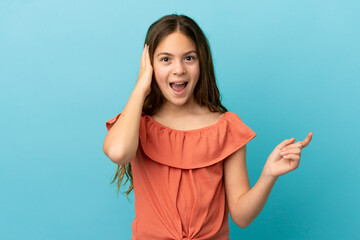 Little caucasian girl isolated on blue background surprised and pointing finger to the side