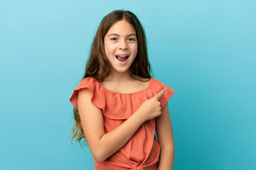 Little caucasian girl isolated on blue background surprised and pointing side