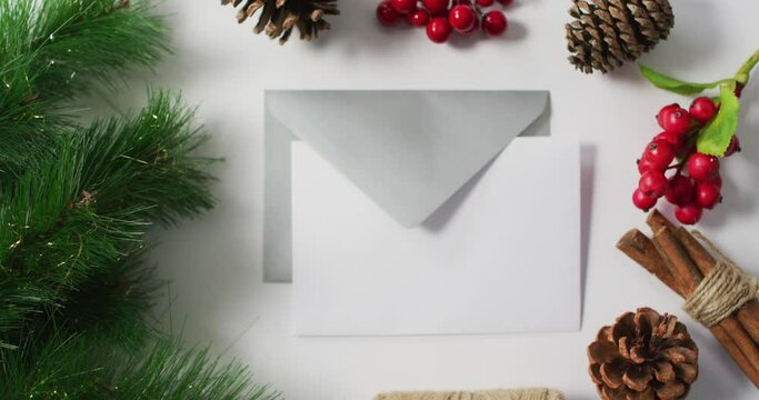 Video of christmas pine cones, tree and red berry decorations with envelopes on white background