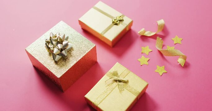 Video of wrapped gold presents and stars on pink background