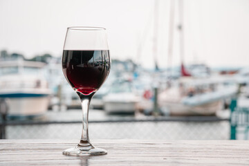 Close up of glass of red wine on a restaurant table outdoors with boats in harbor in background. Selective focus with background blur and copy space.