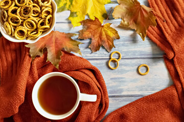 Autumn composition, a cup of hot tea, a warm terracotta scarf, fallen leaves and drying on the background of a blue wooden table. Flat lay