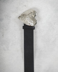 Beautiful black leather belt with silver metal buckle in the shape of hearth over a smoky gray background
