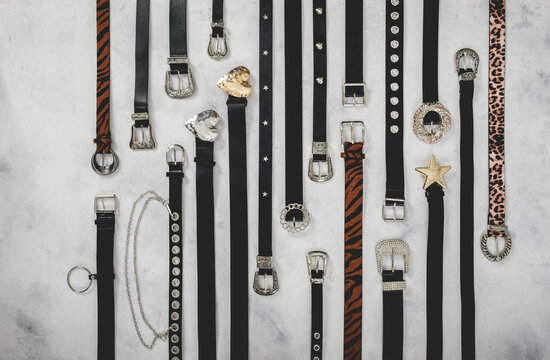 Beautiful collection of black leather belts with golden and silver metal buckles in diverse shapes over a smoky gray background