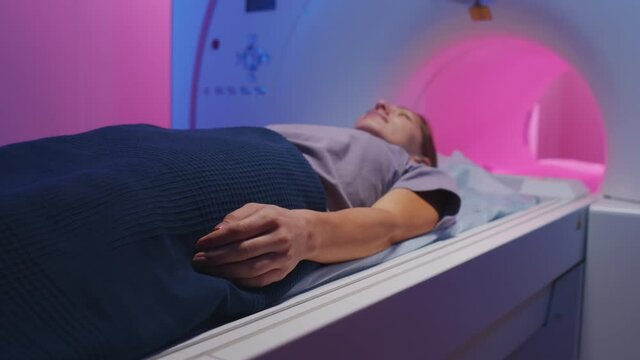 Slowmo shot of young woman having MRI scanning procedure in radiology room of modern clinic with blue and purple lighting
