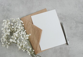 Blank greeting card, envelope and white flowers bouquet on gray concrete background top view. Flat lay. Greeting card mockup, sheet paper card for text.