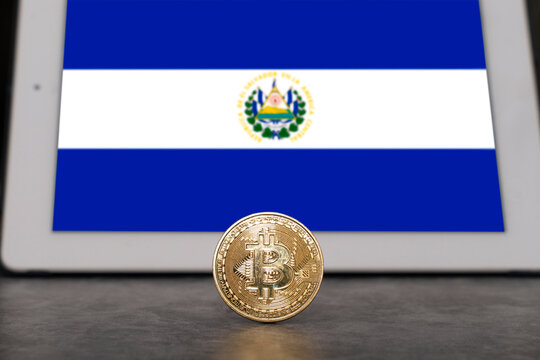 bitcoin currency in the foreground with a tablet with the flag of El Salvador on the screen out of focus. First country in the world to adopt bitcoin as legal tender.