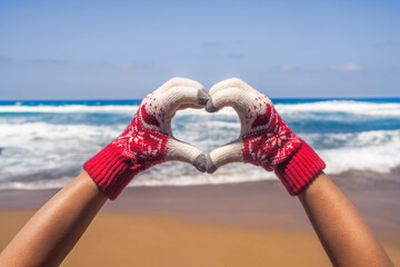 Christmas sea holiday. Happy woman in gloves showing heart shape from hand and relaxing on paradise beach island getaway. New year