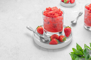 Strawberry granita with mint sicilian frozen summer dessert in glass on a white plate on light grey stone background with copy space. Horizontal orientation. Selective focus.