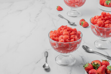 Sicilian (Italy) strawberry granita, frozen summer dessert in glass on marble stone background with copy space, selective focus. Made from water, sugar, and fruit. Horizontal orientation.