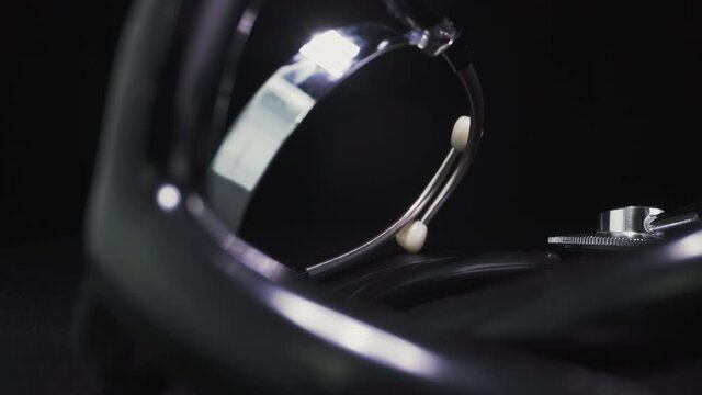 CU, macro shot, dolly cam: motion past shiny modern stethoscope lying on table in clinic on black background extreme close view