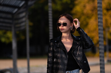 Portrait of a girl with short hair in a leather jacket in the autumn forest. Young hipster or...