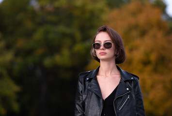 Portrait of a girl with short hair in a leather jacket in the autumn forest. Young hipster or...