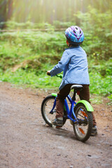 a small child in a helmet learns to ride a two-wheeled bicycle on forest paths. joint time of parents and children, active recreation