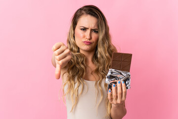 Young Brazilian woman isolated on pink background taking a chocolate tablet making bad signal