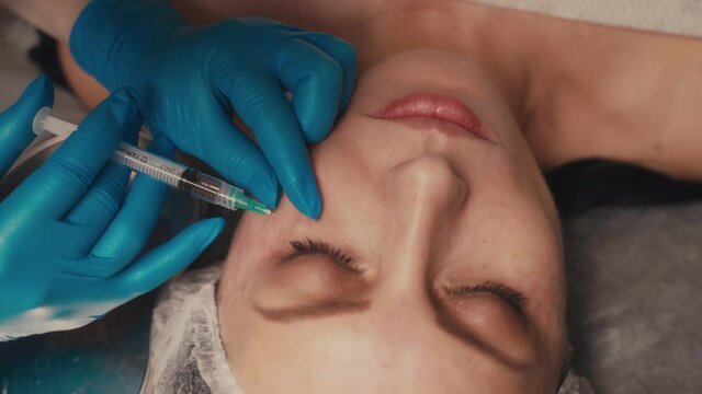 Beauty and injections concept. Experienced beautician entering subcutaneous prick with required active components into female face for tightening and lifting.