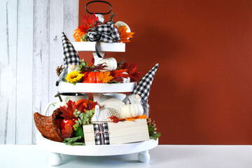Thanksgiving Farmhouse 3 three tier tray decorated with turkey, stack of books, white and ornage pumpkins, black plaid gnomes and autumn fall leaves. Negative copy space.