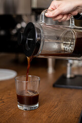 Pouring fresh aromatic coffee from glass kettle in cup on brown background. Brew alternative coffee, v60, French press, filter coffee. Barista prepares filtered coffee.