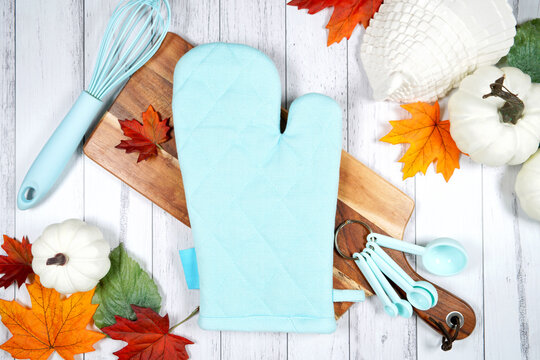 Oven glove kitchen potholder product mockup. Thanksgiving farmhouse theme with turkey, white pumpkins and autumn fall leaves, on a white wood background. Negative copy space.