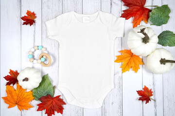 Baby romper jumpsuit onesie product mockup. Thanksgiving farmhouse theme with turkey, white pumpkins and autumn fall leaves, on a white wood background. Negative copy space.