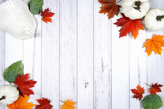 Thanksgiving flatlay framed border backdrop with white pumpkins, autumn leaves, turkey, on a white wood background. Creative composition layout with negative copy space.
