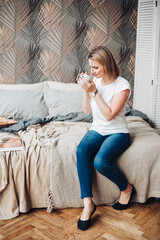 Beautiful girl sits on her bed, reads an interesting book, enjoys of her life and smiles