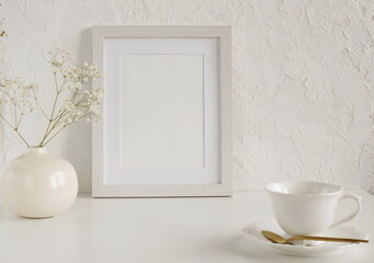 Fototapeta na wymiar Frame mockup on white table, modern ceramic vase with dry flowers, cup coffee.Neutral color. Photo frame, poster template on white textured wall background. Scandinavian interior. Copy space.