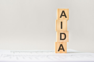 word AIDA with wood building blocks, light gray background. document with numbers on background, business concept. space for text in right. front view.