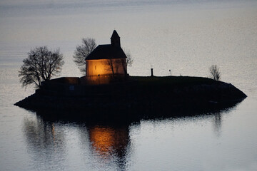 old lit up stone church on island in the lake baie st michel serre ponçon france at dusk with mirror reflection