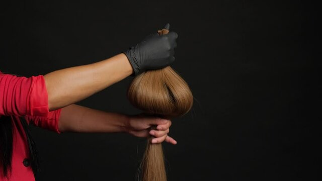 Preparation for hair extension. Girl holding hair in her hand on a black background close-up.