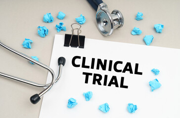 On the table is a stethoscope, a pen, blue crumpled pieces of paper and a sign with the inscription - CLINICAL TRIAL