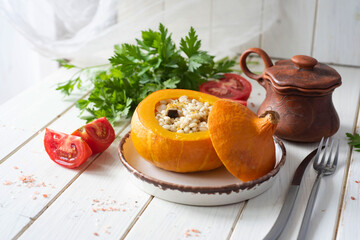 Dinner dish: pumpkin stuffed with pearl barley with vegetables on a white plate on a white background. Close-up.