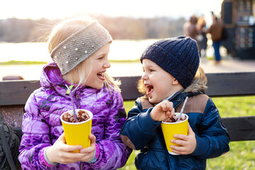 Two cute adorable siblings children sitting on bench drink delicious yummy hot chocolate, tea cocoa...