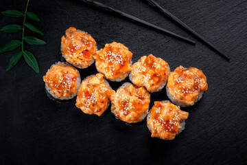 A set of spicy sushi rolls with baked salmon and teriyaki sauce. Maki rolls with nori on a black stone background, top view