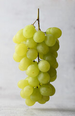 Bunch of white grapes suspended in the air, stone light background.