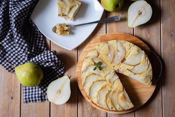 Sweet dessert: pear pie on a wooden platter and a piece of pie on a plate on a wooden table. Top view