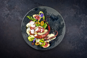Modern style Italian polpo alla griglia su crema di patate with barbecued octopus, potato creme and fresh fruits as top view on a Nordic design plate with copy space