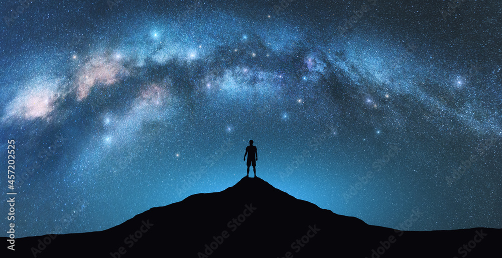 Wall mural milky way arch and man on the mountain peak at starry night. silhouette of alone guy, blue sky with 