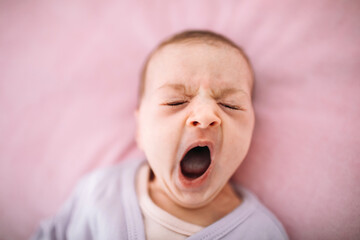 Cute newborn baby yawn before sleep. Portrait of newborn baby on pink background.