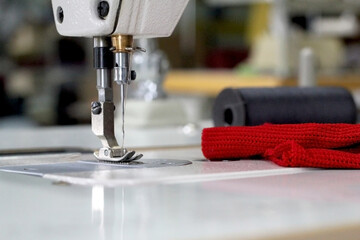 Close-up of the sewing machine mechanism. Next to it is a piece of red cloth and a gray spool of thread.
