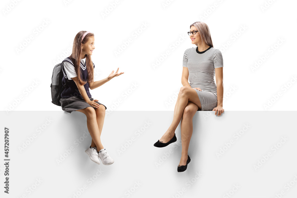 Wall mural Schoolgirl sitting on a blank panel and talking to a young blond woman