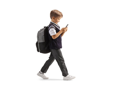 Full length profile shot of a schoolboy walking and typing on a smartphone