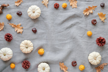 Autumn background with natural pumpkins and dry oak leaves. Flat lay, top view on grey uncolored linen textile. Geometric Fall background with copy-space. Simple, minimal seasonal decorations..