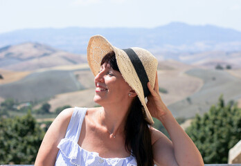 beautiful girl in a straw hat and a sundress on the background of the italian landscape 