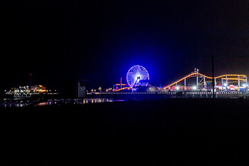 The lights of the Santa Monica Pier, the Ferris wheel and the Rollercoaster reflected in the water of the Pacific Ocean on Santa Monica Beach.