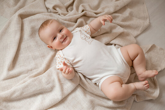 cute baby in a bodysuit is lying on his back on the wooden floor with a blanket at home. High quality photo