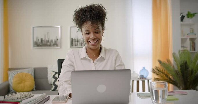 Video Conference Call at Home Office. Lateral Dolly of Happy Young African American Woman Working or Studying on Laptop Computer from Home. Online Learning or Teleworking Concept.