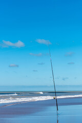 Fishing rod with fishing reel on the beach on a beautiful sunny day. Vertical photo