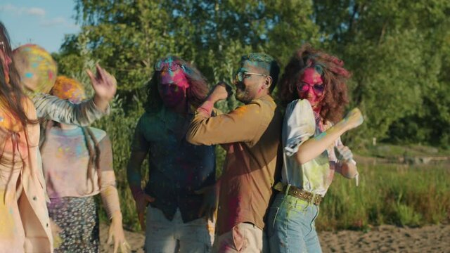 Excited men and women covered with powder paint are dancing having fun at Holi party on sunny summer day. Festivals and carefree young people concept.