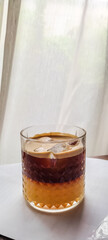 Cold americano coffee with orange juice in glass with transparent curtains in background